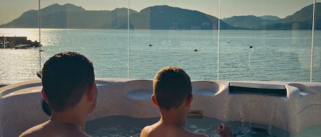 Deux personnes dans un jacuzzi, avec vue sur une étendue d’eau calme et des montagnes lointaines.
