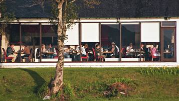 En restaurang med uteservering, ett träd i förgrunden och en byggnad i tegel i bakgrunden.