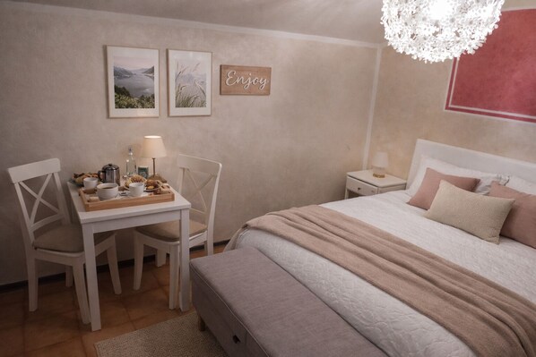 A cozy bedroom with a bed, a bedside table with a lamp, a desk with a chair, and two framed pictures on the wall.