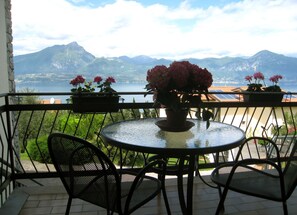 A balcony with a round table and chairs, potted plants, and a view of mountains and a body of water. - B&B Musik Suite with a View of Lake Garda (Torri del Benaco)