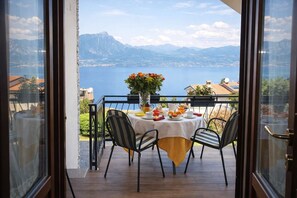 A balcony with a table set for breakfast, overlooking a lake and mountains.