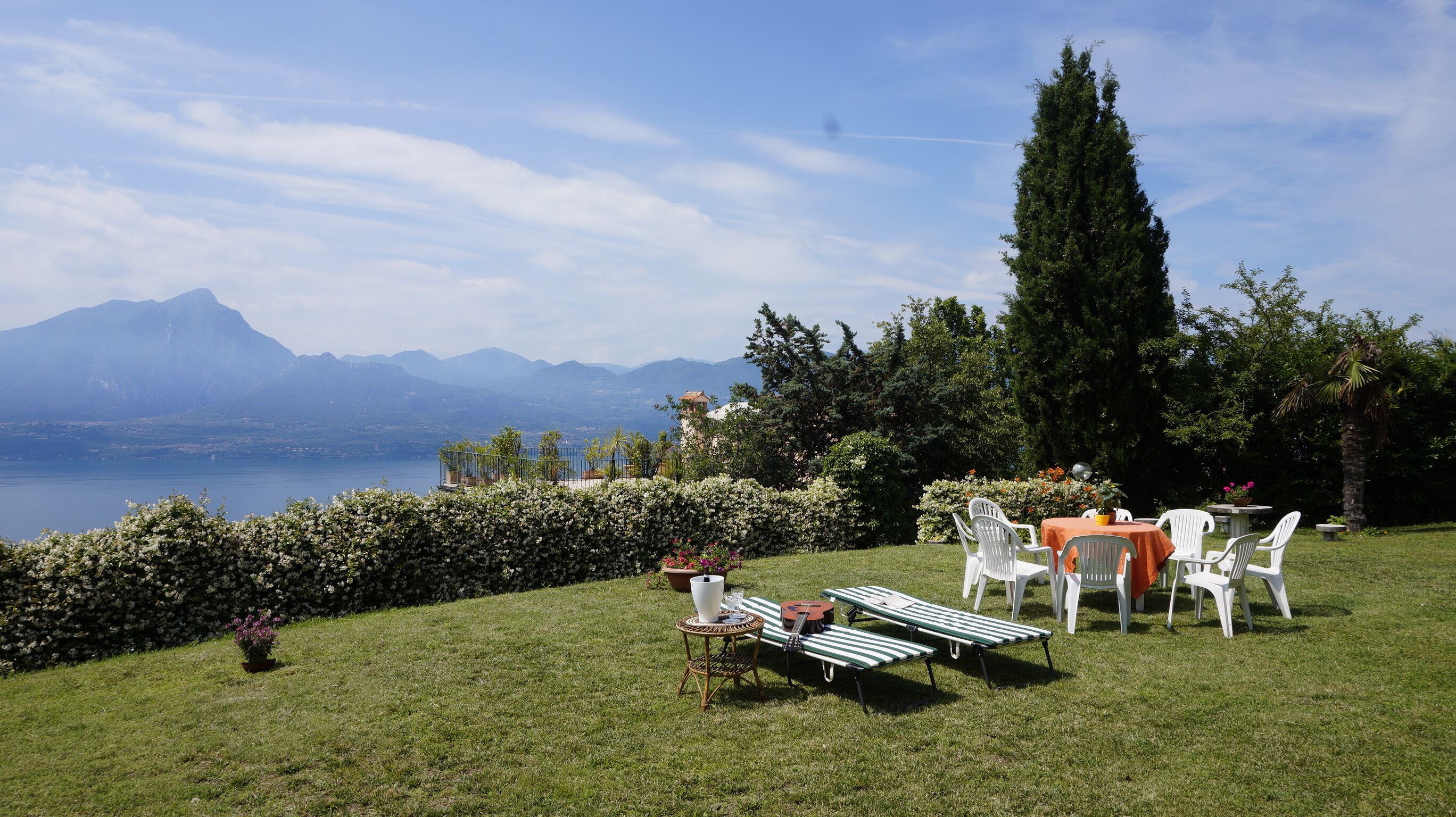 Un espace extérieur verdoyant avec une table et des chaises, un petit jardin et une vue sur les montagnes et un lac.