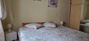 Un dormitorio con cama, dos lámparas de noche, una mesita de noche, un espejo y un cuadro con motivos florales en la pared.
