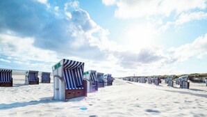 A beach with rows of striped beach chairs and umbrellas, a sandy path, and a clear sky. - 🌊 Holiday home for 6 in Grömitz | 2 bathrooms, garden & beach chair on the beach (Grömitz)