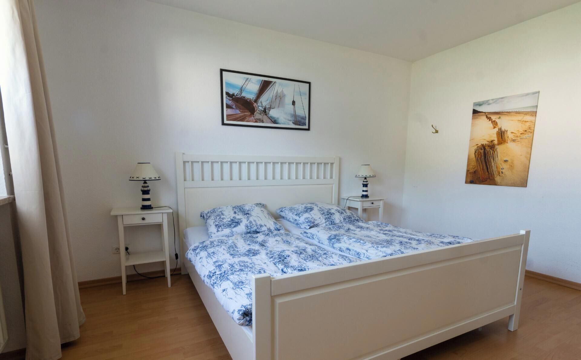 A bedroom with a white bed, two bedside tables with lamps, and two wall-mounted paintings.