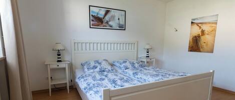 A bedroom with a white bed, two bedside tables with lamps, and two wall-mounted paintings.