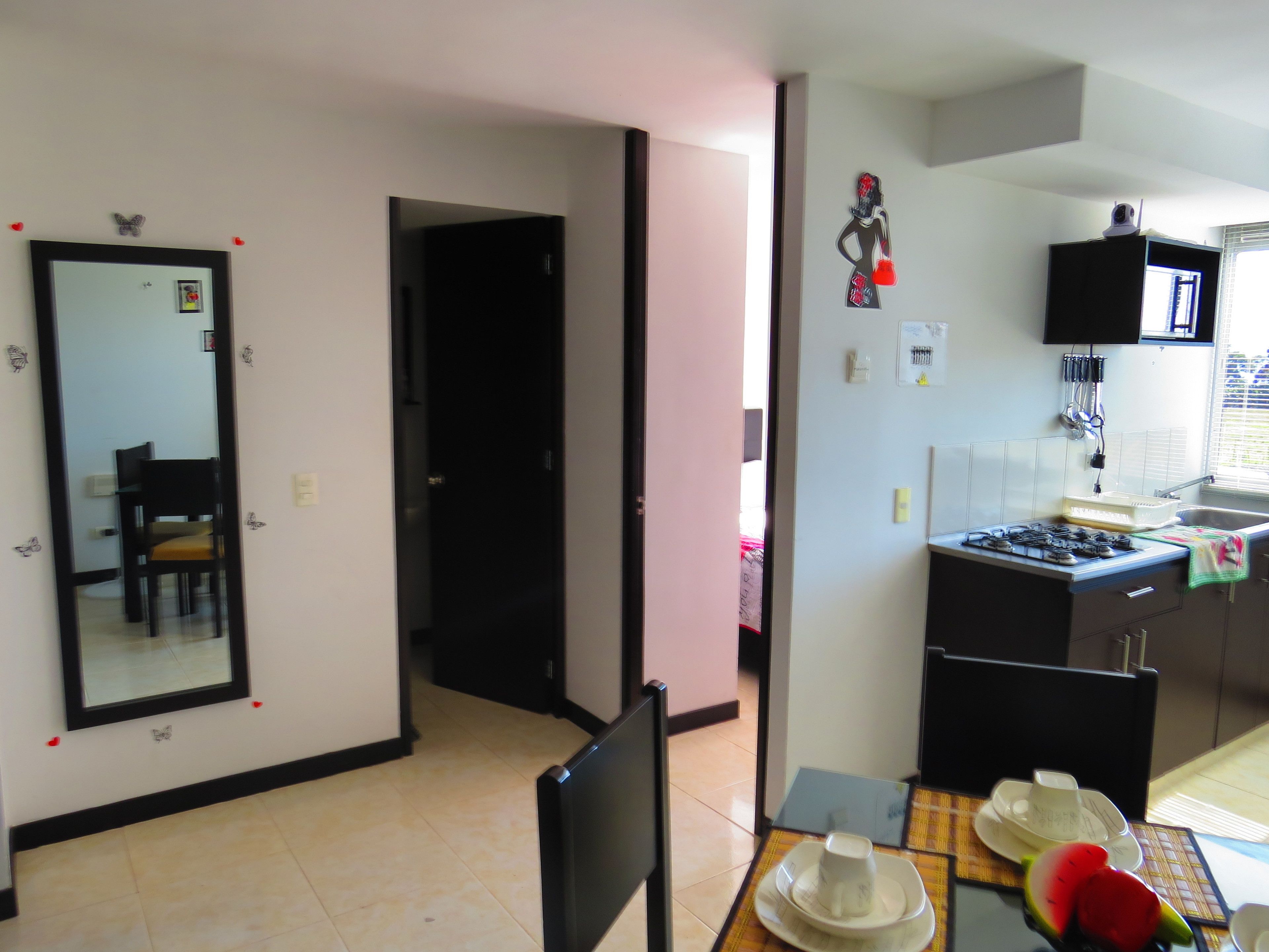 A compact kitchen with a dining area, a mirror, and a small dining table with plates and a cup.