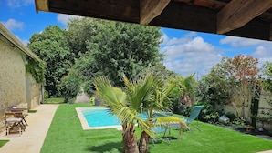 Un patio trasero con piscina, césped artificial, una palmera y un muro de piedra.