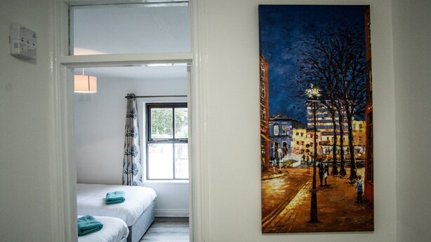 Une chambre d’hôtel avec un lit, une fenêtre et un tableau représentant une rue de la ville de nuit.