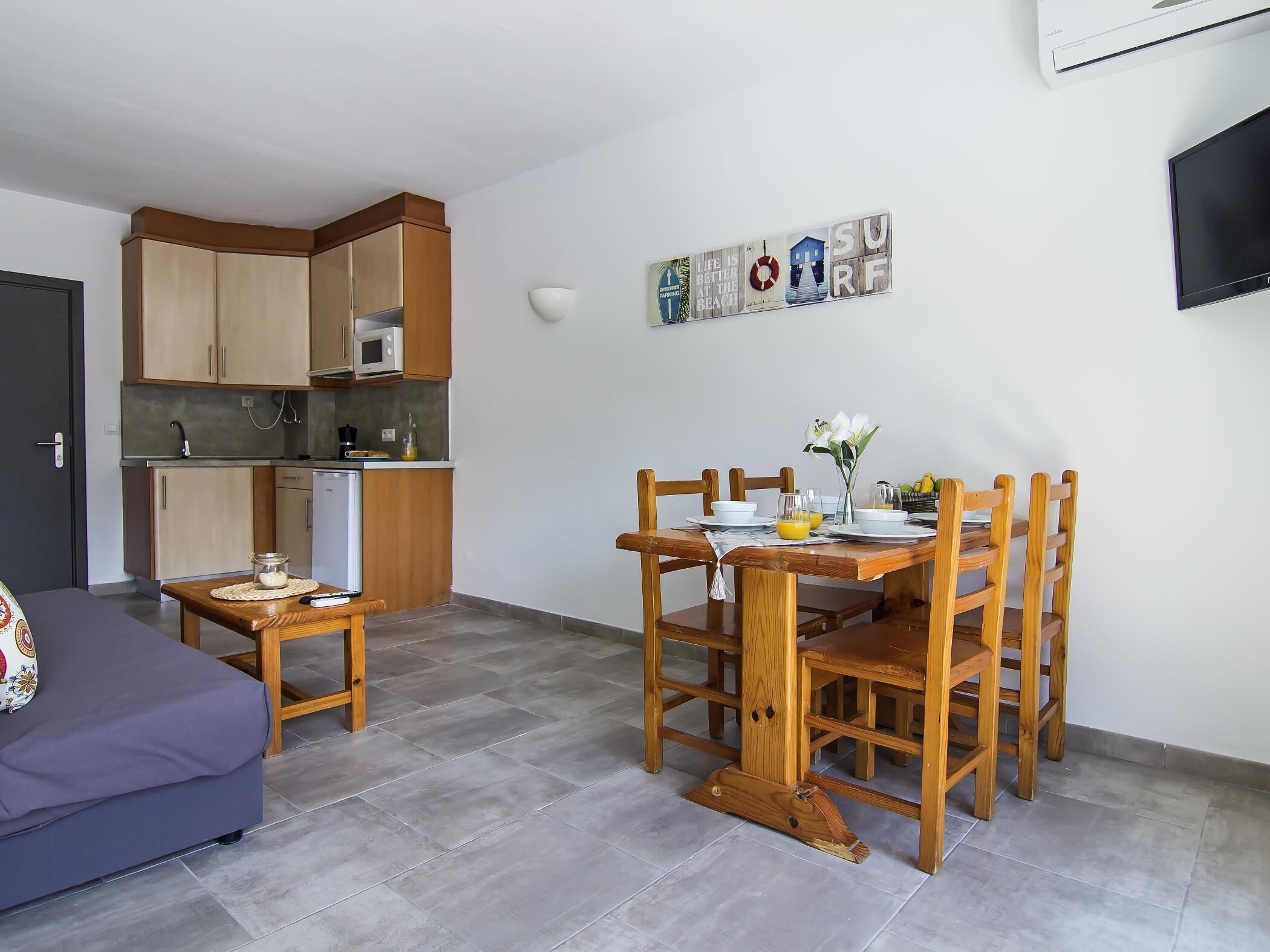 A compact living space with a kitchenette, a dining area with wooden chairs and a table, and a sofa.