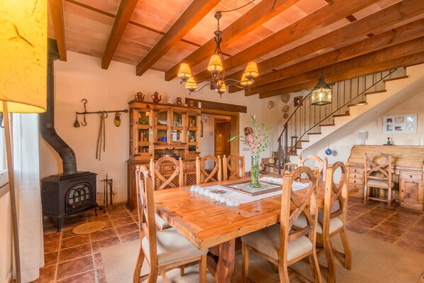 A rustic dining area with a wooden table and chairs, a chandelier, and a staircase leading upstairs.