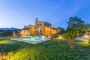 A two-story house with a swimming pool, outdoor seating, and a well-maintained lawn.