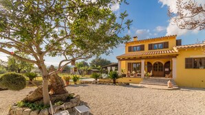 A yellow building with a tiled roof, a stone pathway, and a tree with hanging ornaments. - Sa Tanqueta Rustica, Country House 5StarsHome Mallorca (Inca)