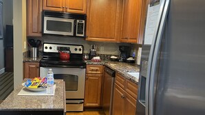 Una cocina con armarios de madera, un refrigerador de acero inoxidable, un microondas, una estufa y una cafetera.