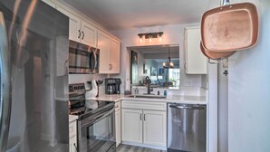 A modern kitchen with white cabinets, stainless steel appliances, and a copper pan hanging on the wall.