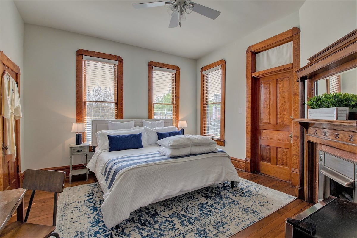 A bedroom with a bed, nightstands, a chair, a wooden door, and a fireplace.