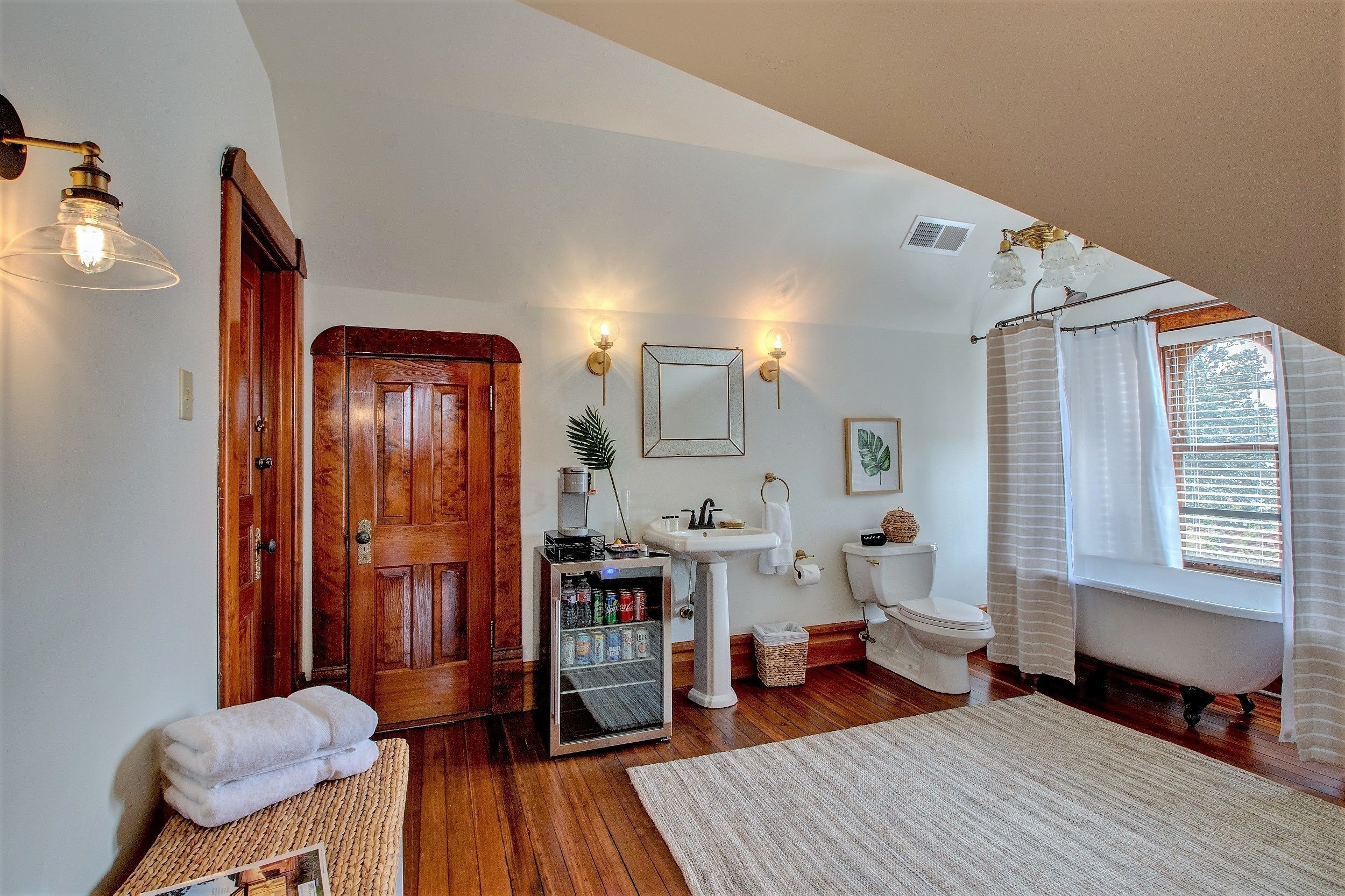 A bathroom with a wooden door, a white sink, a toilet, a bathtub, and a window with curtains.