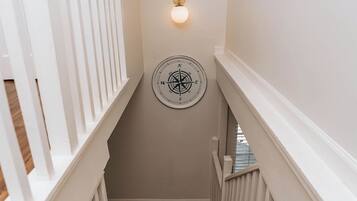 A staircase with white railings and a wooden floor, leading to a room with a wall-mounted light fixture and a compass decoration.