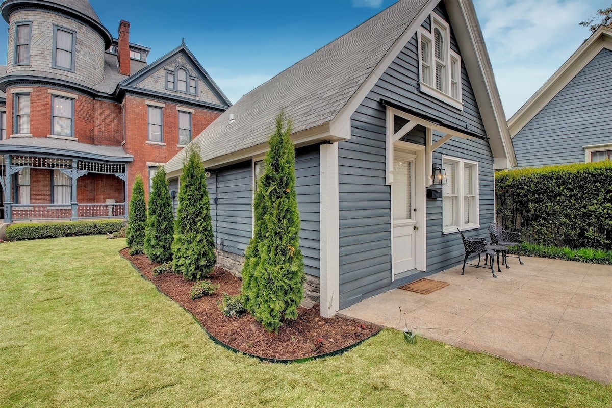 A two-story house with a grey exterior, a front porch with a bench, and a small patio area.