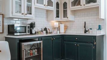 Una cocina con armarios blancos, microondas, cafetera y refrigerador.