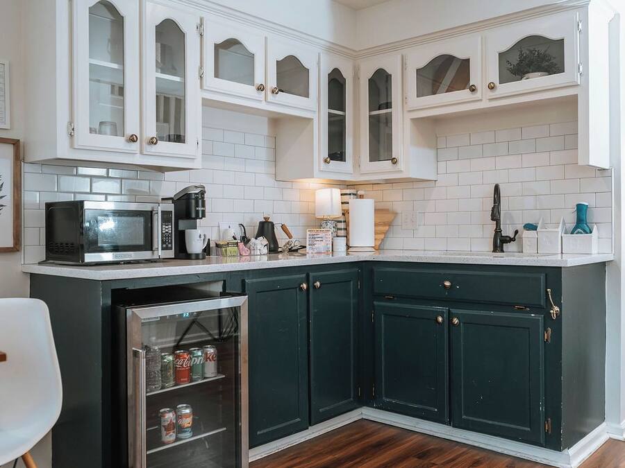Una cocina con armarios blancos, microondas, cafetera y refrigerador.
