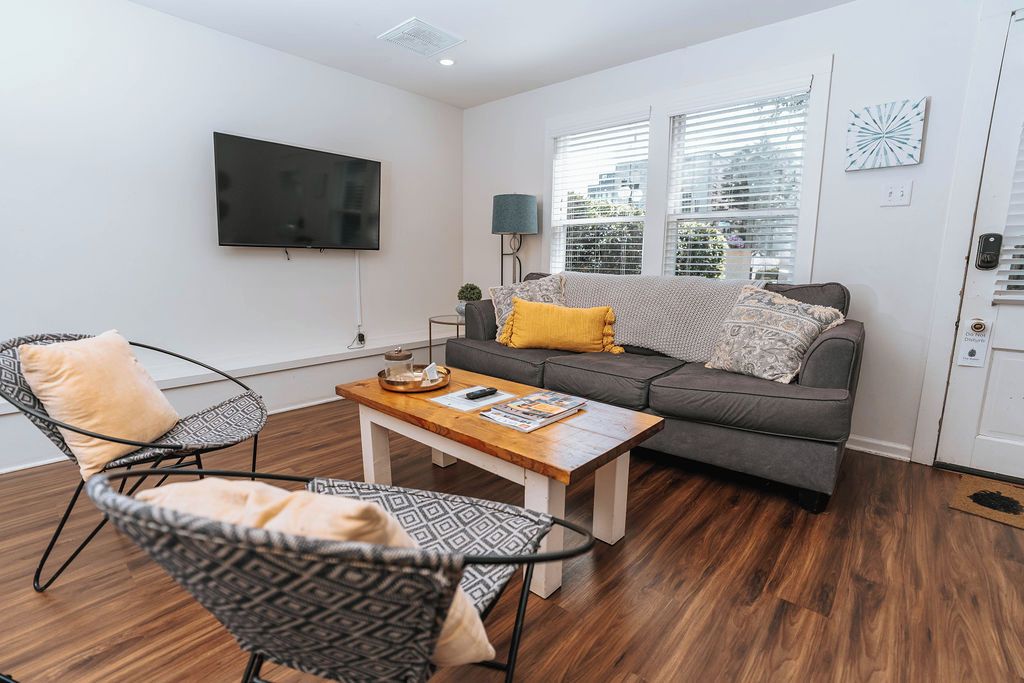 A living room with a grey sofa, patterned chairs, a wooden coffee table, and a flat-screen TV mounted on the wall.