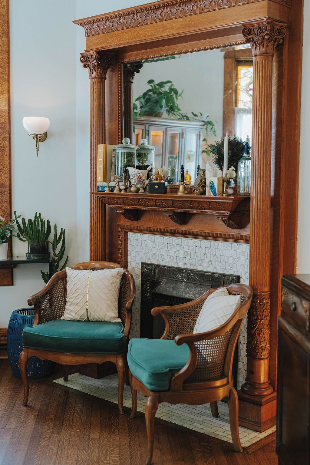 A room with a fireplace, two upholstered chairs, a mirror, and various decorative items on the mantel.