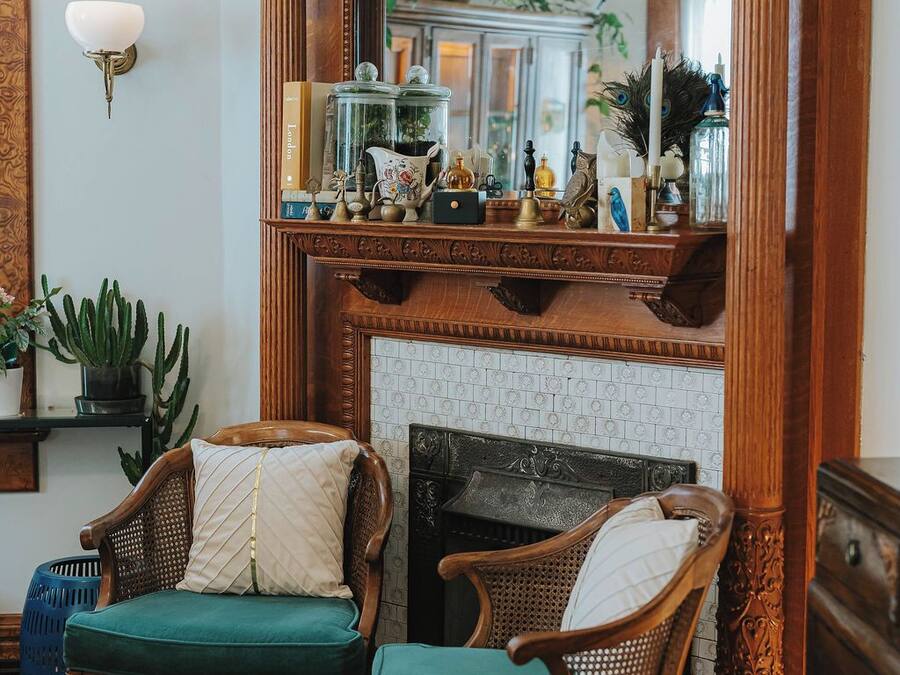 A room with a fireplace, two upholstered chairs, a mirror, and various decorative items on the mantel.