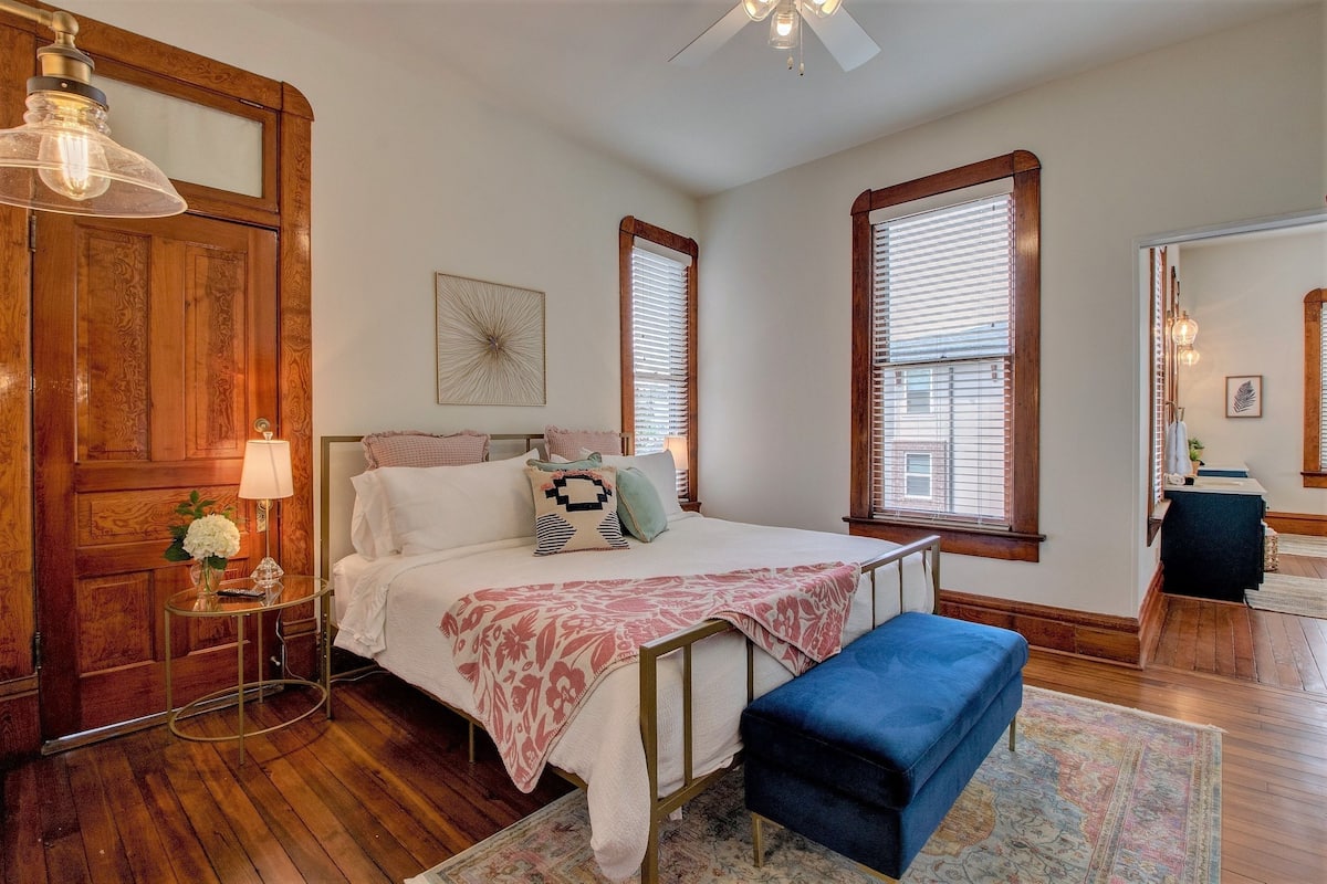 A bedroom with a bed, bedside table, lamp, and a large mirror.