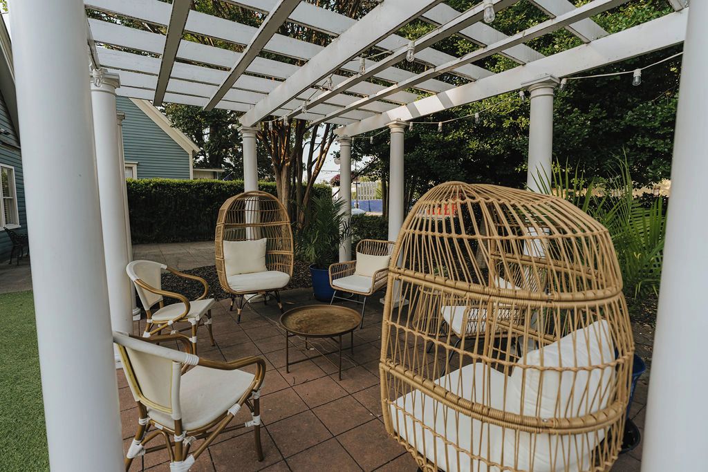 Ein überdachter Patio-Bereich mit Korbmöbeln, darunter Stühle und ein Hängesessel, sowie einer Pergola.