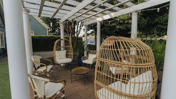 Ein überdachter Patio-Bereich mit Korbmöbeln, darunter Stühle und ein Hängesessel, sowie einer Pergola.
