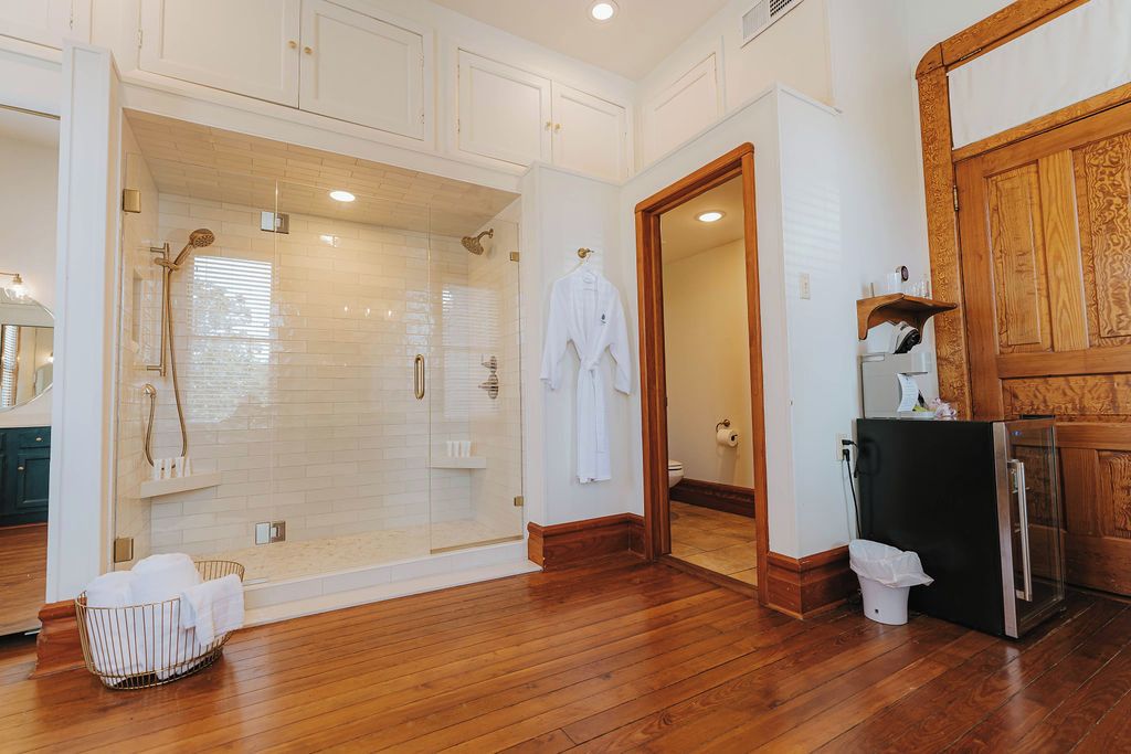 A spacious bathroom with a walk-in shower, a wooden floor, and a white tiled wall.