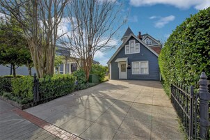 Uma casa residencial com jardim frontal, calçada pavimentada e cerca de metal preto.