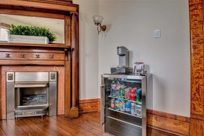 A room with a built-in fireplace, a minibar with beverages, and a wall-mounted coffee machine. - The Baker (North Little Rock)