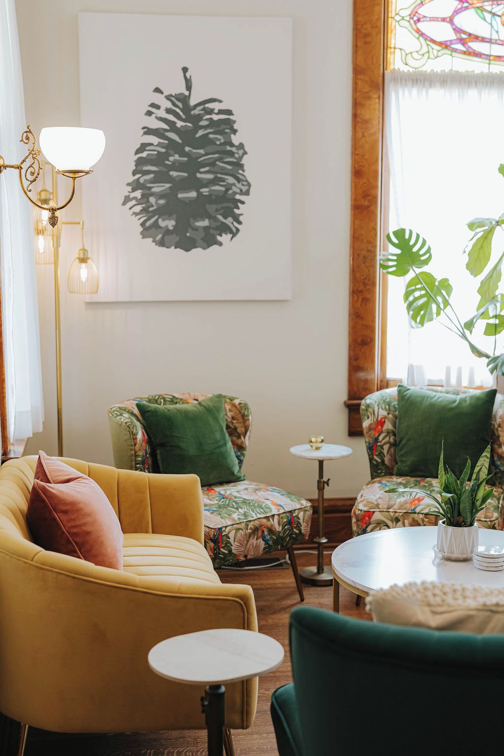 Una habitación con un sofá amarillo, sillones verdes, una mesita redonda y un ventanal con una planta.