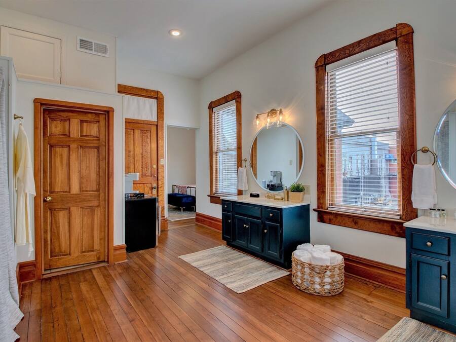 A bathroom with wooden flooring, a vanity with a mirror, and a window with blinds.