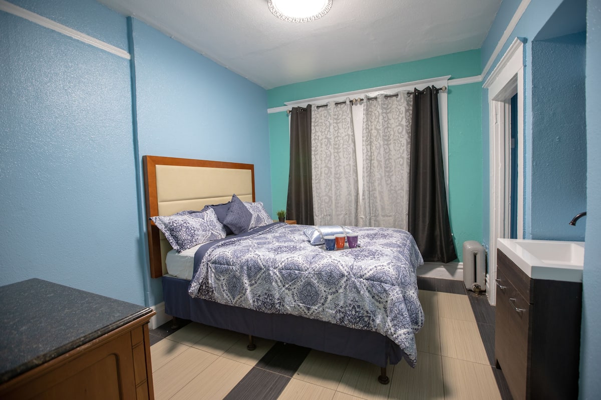 A bedroom with a bed, a bedside table, a dresser, and a window with curtains.