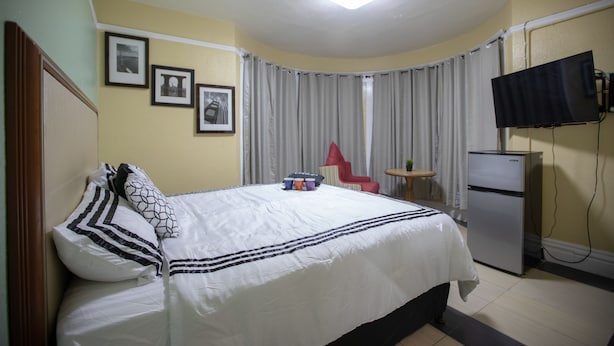 Habitación de hotel con cama, televisión, refrigerador, una silla roja y cuadros en la pared.
