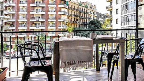Un balcon avec une table, des chaises et un pot de fleurs.