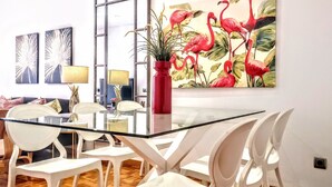 Un espace repas moderne avec une table en verre, des chaises blanches et un vase rouge contenant une plante.
