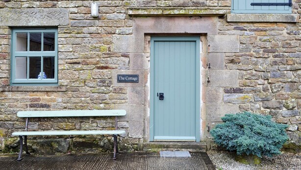 A stone cottage with a green door, a bench, and a sign reading "The Cottage".