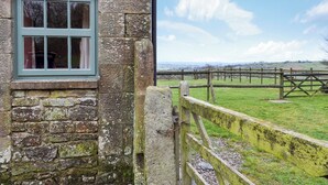 A stone building with a window and a wooden gate leading to a grassy field.