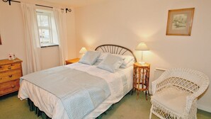 A bedroom with a bed, two bedside tables, a chair, a window with curtains, and a wall-mounted picture.
