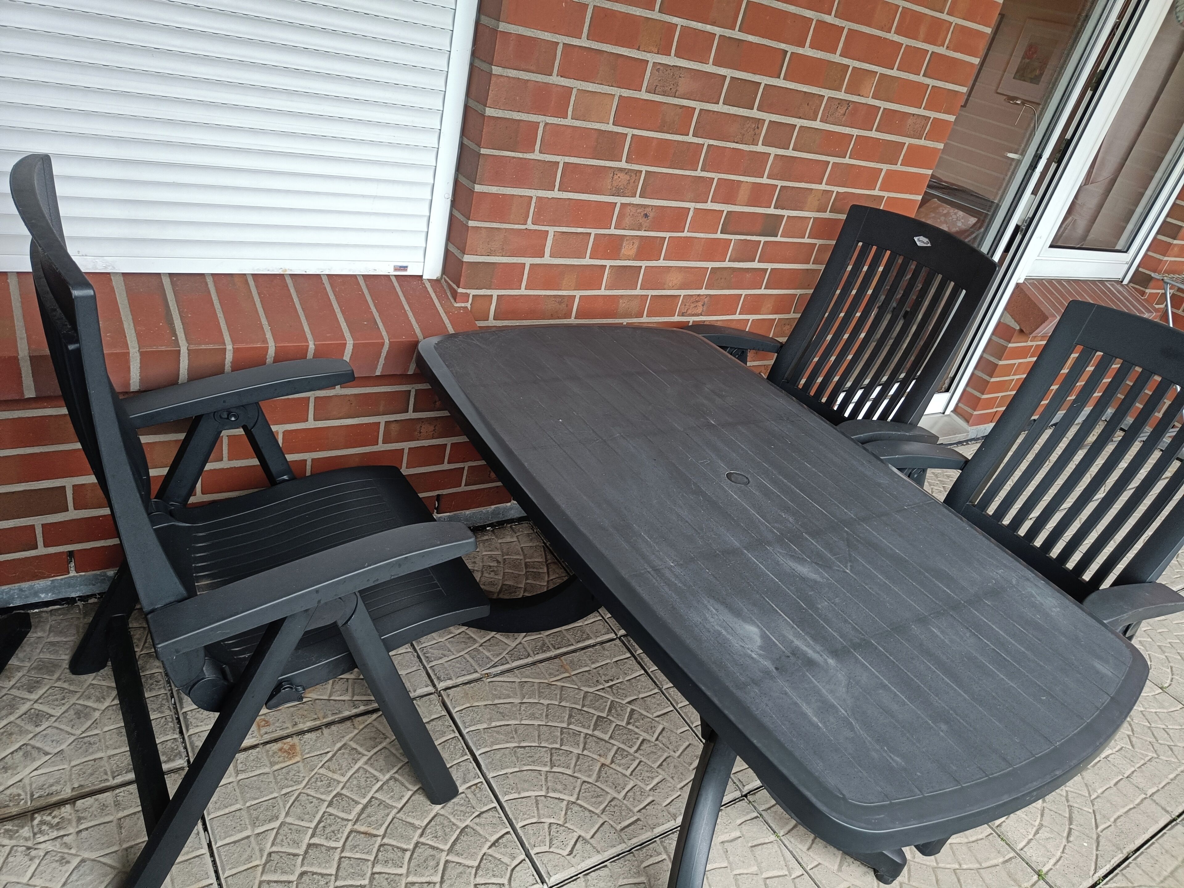A patio with a table and chairs, a brick wall, and a sliding door.