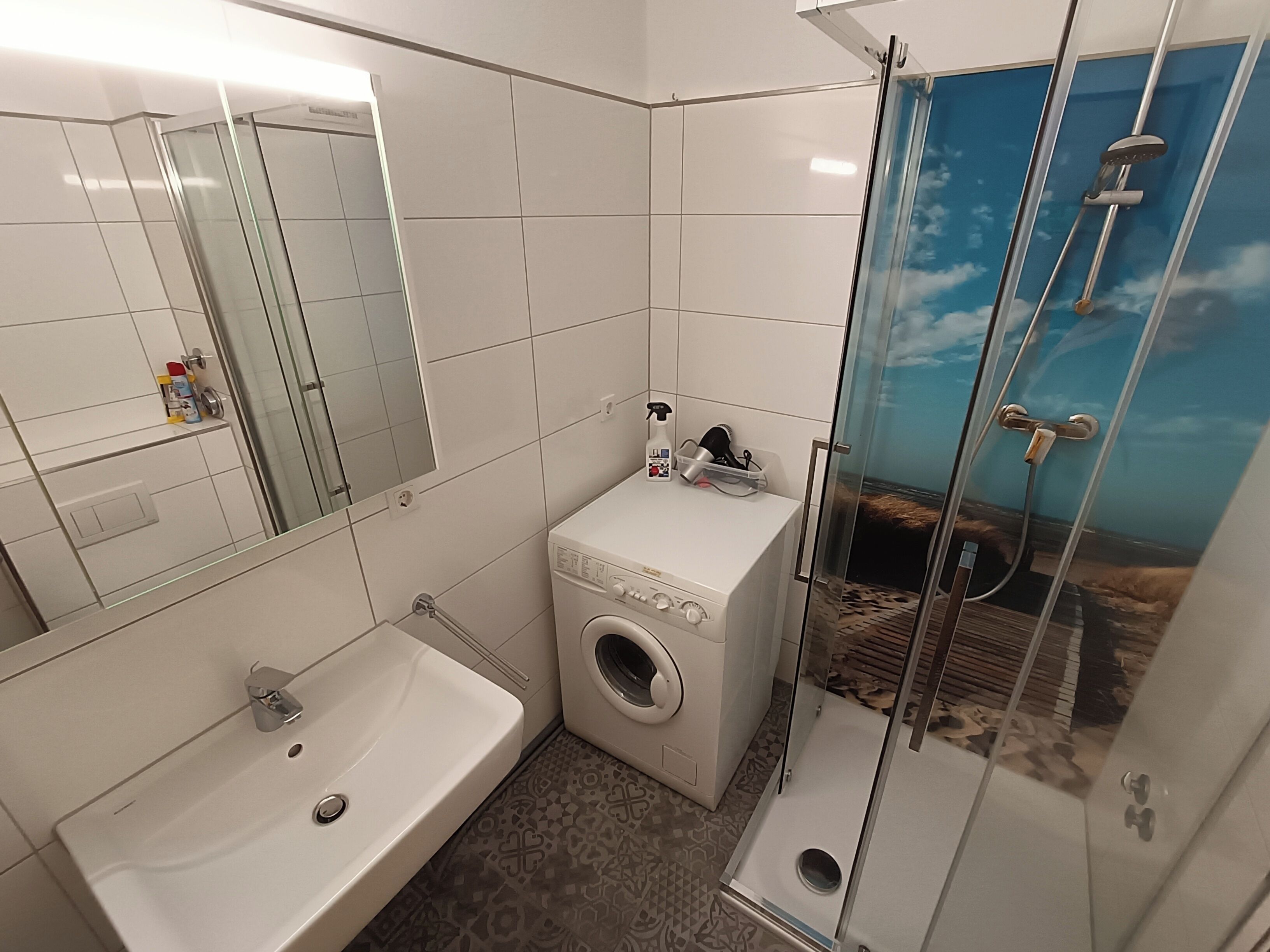 A bathroom with a sink, washing machine, and glass shower enclosure.