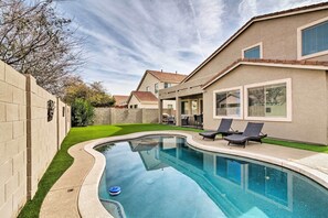 Une piscine à bord incurvé, entourée d’une terrasse dallée et d’une pelouse.