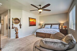 Une chambre à coucher avec un lit, deux tables de chevet avec des lampes, un ventilateur de plafond et une grande fenêtre avec des stores.