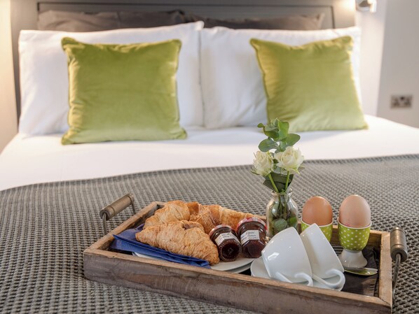 A breakfast tray with croissants, jam, eggs, and a vase of flowers on a bed with green pillows.