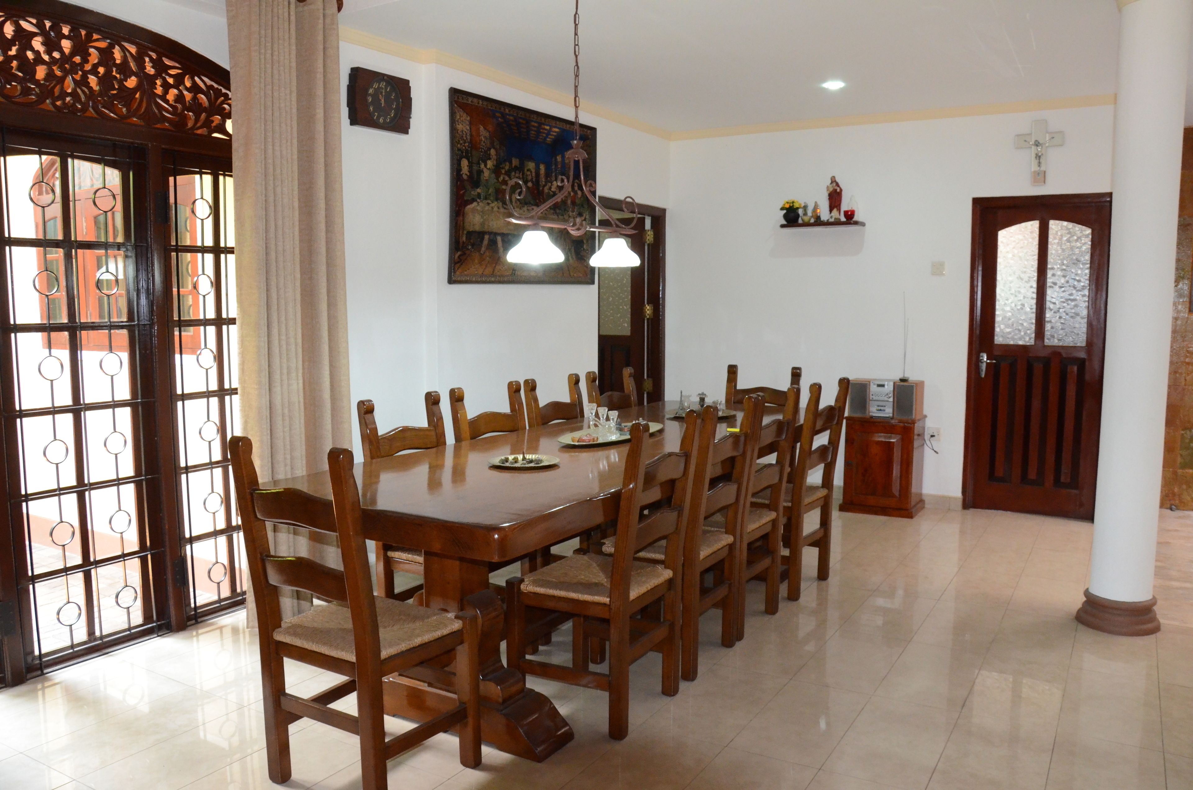Uma sala de jantar com mesa e cadeiras de madeira, um lustre e uma porta com uma cruz em cima.