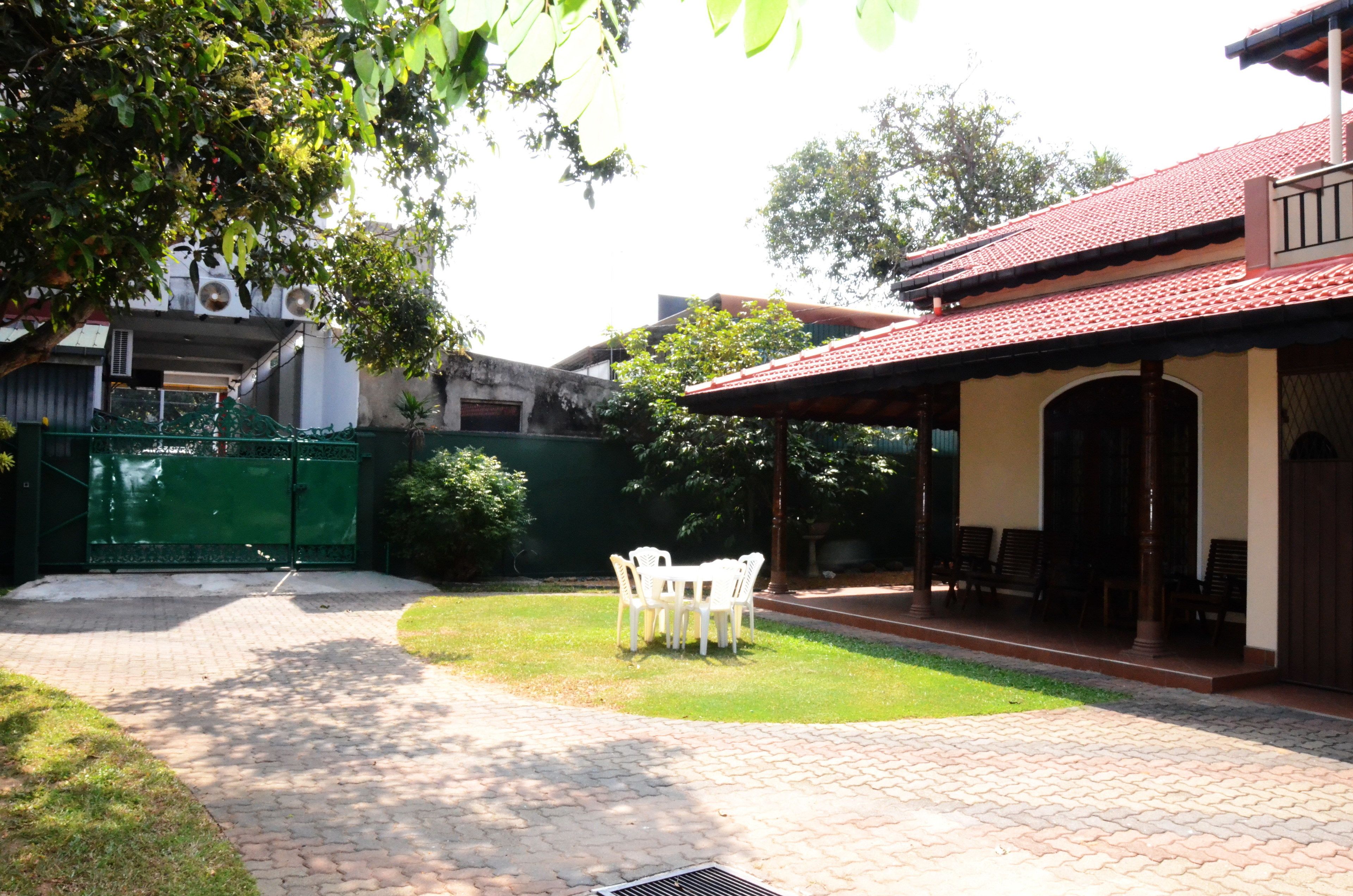 Un patio con zona pavimentada, un portón verde y un edificio con tejado de tejas y una zona de estar cubierta.